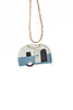 A hand-painted metal Christmas ornament shaped like a retro semi-trailer caravan, featuring a white top half, a light blue bottom half, and colourful bunting, hanging from a natural jute twine string against a plain white background.