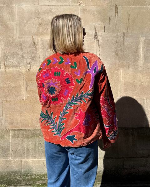 Person wearing a colorful jacket with floral patterns standing against a stone wall.