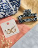 Gold hoop earrings on a card with a blue and black marble hair clip on a textured surface.